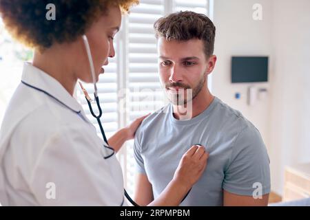 Weibliche Krankenschwester trägt Uniform und hört auf die Brust des männlichen Patienten im privaten Krankenhauszimmer Stockfoto