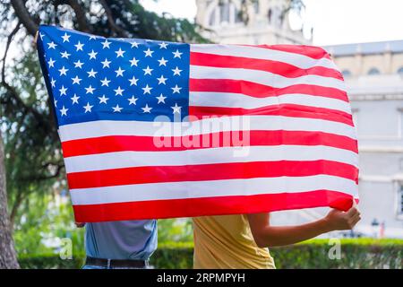 Ein Paar in der Stadt mit usa-Flagge, Jungen und Mädchen auf dem Rücken. Patrioten stolz auf ihre Nation, Unabhängigkeitstag Stockfoto