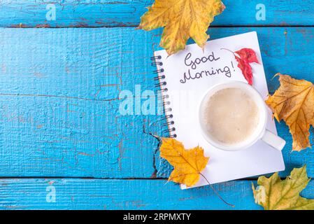 Kaffeebecher mit einem Strauß herbstlicher Herbstblätter und Blumen, Noten Guten Morgen auf türkisblauem Holztisch, von oben, gemütliches, wunderschönes Herbstfrühstück Stockfoto