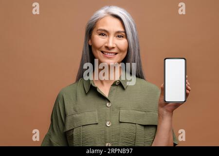 Charmante asiatische Frau im mittleren Alter der 40er Jahre zeigt Smartphone mit einem leeren weißen Bildschirm, mobile App-Werbung isoliert, Kopierplatz Stockfoto