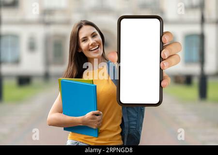 Schulungsangebot. Schöne Lächelnde Schülerin, Die Ein Leeres Smartphone Vorführt, Während Sie Draußen Steht Stockfoto