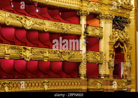 Ein Operntheater mit einer kunstvoll verzierten Bühne mit einem gemusterten roten Teppich und passenden Stühlen im Vordergrund mit goldenen Dekorationen Stockfoto