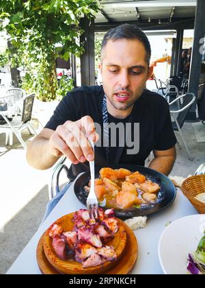 Junger Mann essen Pulpo a la Gallega mit Kartoffeln. Galizische octopus Gerichte. Bekannte Gerichte aus Galizien, Spanien. Stockfoto