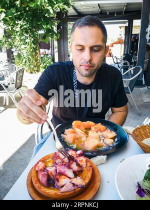 Junger Mann essen Pulpo a la Gallega mit Kartoffeln. Galizische octopus Gerichte. Bekannte Gerichte aus Galizien, Spanien. Stockfoto