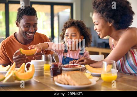 Familienschoß Mit Eltern Und Tochter Zu Hause Beim Frühstück, Das Marmelade Auf Brot Am Tisch Verteilt Stockfoto