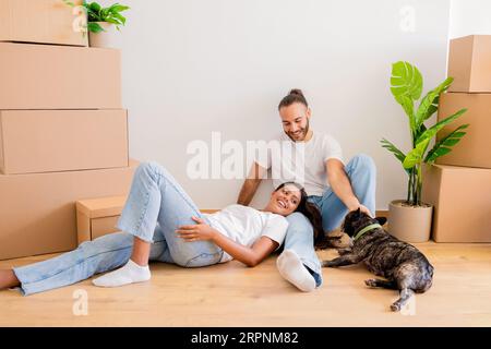 Glückliches junges Paar, das seine neue Wohnung genießt und mit Hund spielt Stockfoto