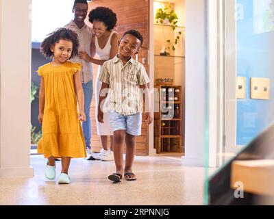 Familie, Die Nach Hause Kommt, Öffnet Die Vordertür Und Kinder Laufen Hinein Stockfoto