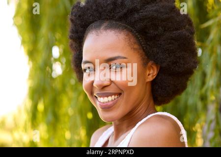 Porträt Der Lächelnden Schönen Frau, Die Am Baum Im Garten Zu Hause Steht Stockfoto