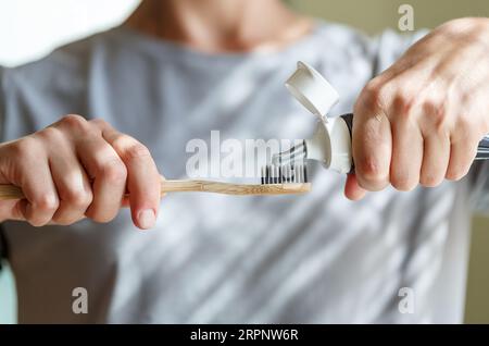 Zahnpasta auf eine Bambuszahnbürste auftragen. Hände, die den Schlauch mit einer Zahnpasta zusammendrücken. Zahnheilkunde und Hygenkonzept. Stockfoto