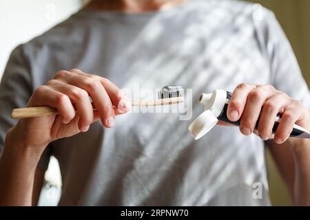 Zahnpasta auf eine Bambuszahnbürste auftragen. Hände, die den Schlauch mit einer Zahnpasta zusammendrücken. Zahnheilkunde und Hygenkonzept. Stockfoto