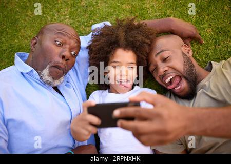Overhead-Aufnahme Von Multi-Generation Male Family Living On Grass Mit Selfie Auf Dem Mobiltelefon Stockfoto