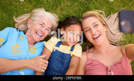 Overhead-Aufnahme Von Multi-Generation Female Family Living On Grass Mit Selfie Auf Dem Handy Stockfoto