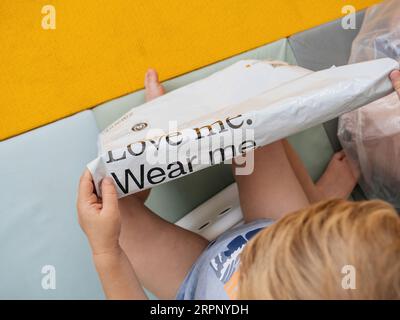 Hamburg, Deutschland - 24. Juli 2023: Kleinkind betrachtet die Bedeutung einer recycelbaren Plastiktüte mit dem Zalando-Logo und dem berührenden Slogan Love Me, Wear Me. Stockfoto