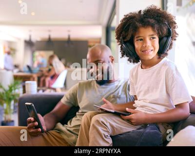 Vater Mit Mobiltelefon Und Sohn Mit Digitalem Tablet Mit Kopfhörern Zu Hause Stockfoto