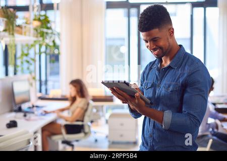 Junger Lächelnder Geschäftsmann Mit Digitalem Tablet Stand Und Arbeit Im Modernen Büro Stockfoto