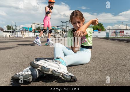 Ein Schulmädchen ohne Schutzausrüstung fiel beim Rollschuhlaufen im Stadion auf den Asphalt. Kinder reiten in einem Skatepark. Gefährlicher Eintritt Stockfoto