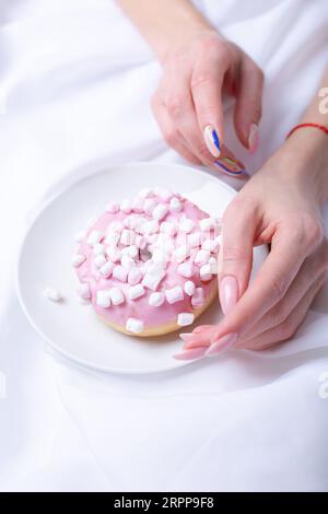 Pinkfarbener Donut und weibliche Hand mit Maniküre Stockfoto