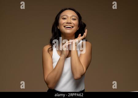 Glückliche asiatische Frau mit dunklen Haaren, die Hände berühren Stockfoto