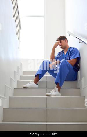 Gestresster Männlicher Arzt Oder Krankenschwester, Die Scrubs Trägt, Sitzt Auf Treppen Im Krankenhaus Stockfoto