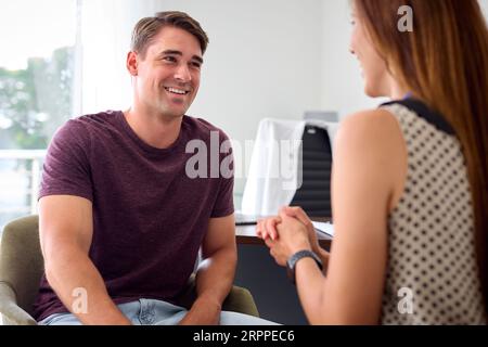 Lächelnder junger Mann bei einem Termin mit Ärztin oder Hausarzt im Büro Stockfoto