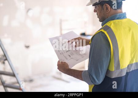 Mann in der Weste prüft die Zeichnung der Wohnung, bevor er mit der Renovierung beginnt Stockfoto