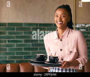 Porträt Der Lächelnden Besitzerin Oder Des Mitarbeiters, Die Tassen Im Café Oder Café Trägt Stockfoto