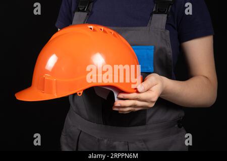 Orangefarbener Schutzhelm in den Händen einer Bastlerin auf schwarzem Hintergrund. Stockfoto