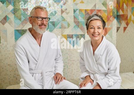 Ein fröhliches Paar mittleren Alters in weißen Bademänteln sitzt in Sauna, Spa und Wellness-Konzept, Hamam Stockfoto