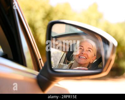 Lächelnde Ältere Weibliche Fahrerin, Die Sich Im Wing Mirror Of Car Spiegelt Und Einen Tagesausflug Nach Draußen Genießt Stockfoto