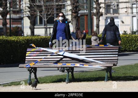 200325 -- BRÜSSEL, 25. März 2020 -- Menschen gehen an Bänken vorbei, die von der Polizei in einem Park in Brüssel, Belgien, am 25. März 2020 mit dem Absperrband gefesselt sind. Bänke in Parks wurden verboten, weil sie sitzen mussten, um zu verhindern, dass sich die Leute versammeln oder zu lange in den Parks bleiben. BELGIEN-BRÜSSEL-COVID-19-PARK-BANK ZhengxHuansong PUBLICATIONxNOTxINxCHN Stockfoto