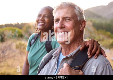 Seniorenpaar Mit Rucksäcken, Die Gemeinsam Auf Dem Land Wandern Stockfoto