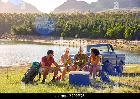 Gruppe Von Freunden Mit Rucksäcken Mit Dem Pick-Up-Truck Auf Road Trip Bier Von Cooler By Lake Trinken Stockfoto