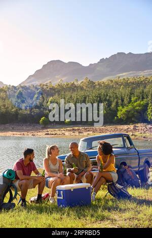 Gruppe Von Freunden Mit Rucksäcken Mit Dem Pick-Up-Truck Auf Road Trip Bier Von Cooler By Lake Trinken Stockfoto