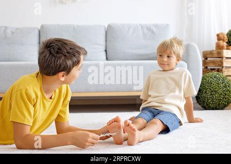 Glückliche positive Kinder, kitzeln auf den Füßen, haben Spaß zusammen, Junge Brüder zu Hause haben einen wunderbaren Tag der Freude zusammen Stockfoto