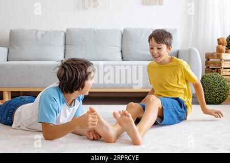 Glückliche positive Kinder, kitzeln auf den Füßen, haben Spaß zusammen, Junge Brüder zu Hause haben einen wunderbaren Tag der Freude zusammen Stockfoto