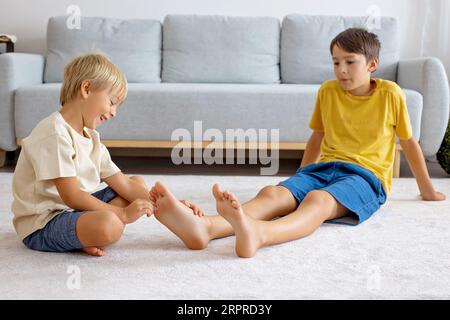 Glückliche positive Kinder, kitzeln auf den Füßen, haben Spaß zusammen, Junge Brüder zu Hause haben einen wunderbaren Tag der Freude zusammen Stockfoto