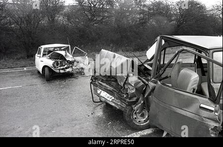 1983, historische, abgestürzte Autos seitlich auf einer nassen Straße liegend, nach einem Kopf auf Smash, Yorkshire, England, Großbritannien. Stockfoto