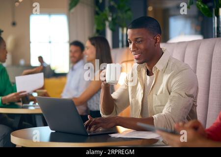 Geschäftsmann, Der Kaffee Trinkt Und Am Laptop Arbeitet, Im Informellen Sitzbereich Des Modernen Büros Stockfoto