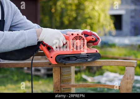 Nahaufnahme des Zimmermanns mit Elektroschleifer zur Restaurierung des alten Stuhls Stockfoto