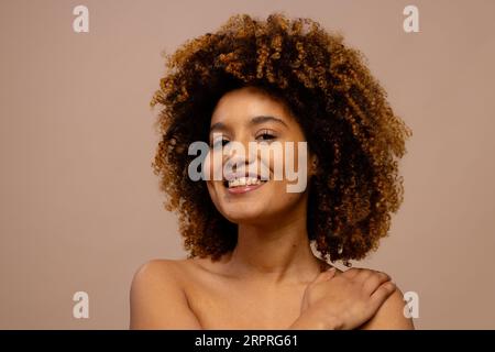 Glückliche birassische Frau mit dunklen lockigen Haaren, lächelnd mit der Hand auf der Schulter Stockfoto