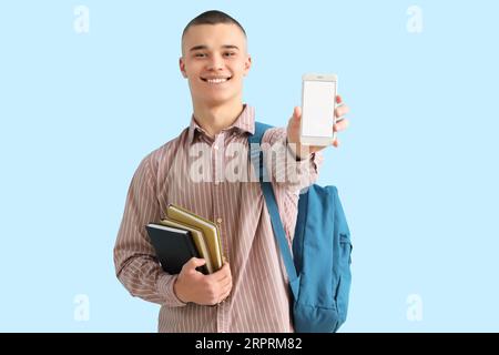 Männlicher Student mit Rucksack, Büchern und Handy auf blauem Hintergrund Stockfoto