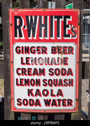 Keramisches Schild für R Whites Softdrinks (Ingwerbier, Limonade, Cremesoda usw.) am Zaun vor dem Bahnhof Horstead Keynes, Sussex, Großbritannien. Stockfoto