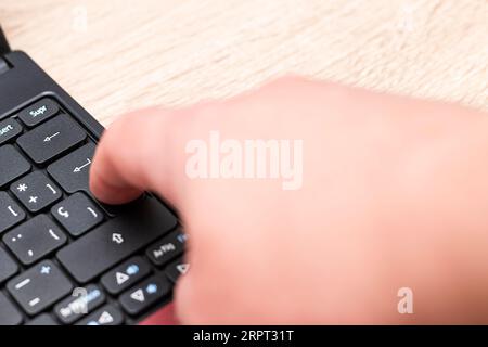 Nahaufnahme des Zeigefingers einer kaukasischen menschlichen Hand, der die Eingabetaste auf einer Laptop-Tastatur über einen Holztisch drückt. Stockfoto