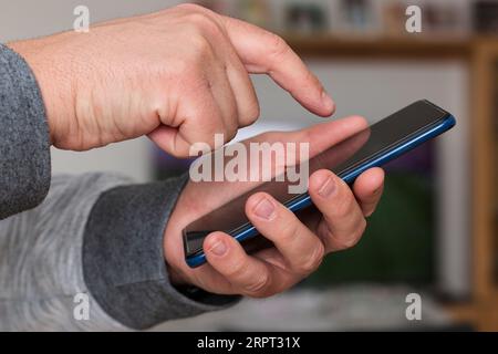 Nahaufnahme einer kaukasischen, nicht erkennbaren Person, die die Hand hält und den Bildschirm eines Mobiltelefons in einem Haus berührt. Stockfoto
