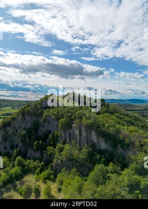 Blick aus der Vogelperspektive auf die steile Klippe auf einem Hügel mit grünen Bäumen, die oben unter blauem Himmel mit Wolken in der italienischen Landschaft wachsen Stockfoto