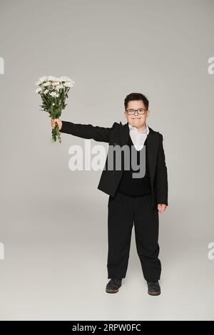 Schuljunge mit Down-Syndrom bei Brille und gleichmäßigem Holmbruch in ausgestreckter Hand auf Grau Stockfoto