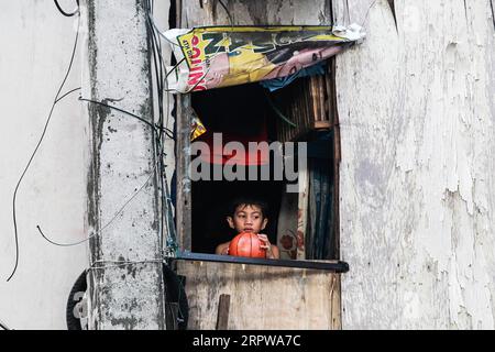 200424 -- PEKING, 24. April 2020 -- Ein Junge hält einen Ball, während er am 23. April 2020 aus dem Fenster seiner Shanty in einem Slum-Gebiet in Quezon City auf den Philippinen schaut. XINHUA FOTOS DES TAGES RouellexUmali PUBLICATIONxNOTxINxCHN Stockfoto