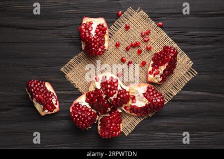 Ein großer Granatapfel mit Reifen, großen, saftigen Samen wird auf einem hölzernen Hintergrund in Stücke zerlegt, Draufsicht, Granatapfelkörner sind verstreut. Stockfoto