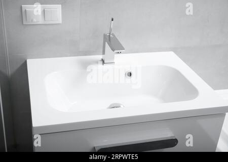 Moderne Badezimmereinrichtung, weißes Waschbecken mit Schubladen, Chromhahn, Steckdose und Schalter an der Wand. Badezimmer mit Waschbecken und Wasserhahn. Stockfoto
