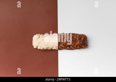 Weiß- und Milchschokolade auf kontrastierenden Hintergründen. Zwei Hälften einer Schokoladentafel mit knusprigen Waffeln. Konzeptionelle Darstellung zweier Gegensätze in t Stockfoto